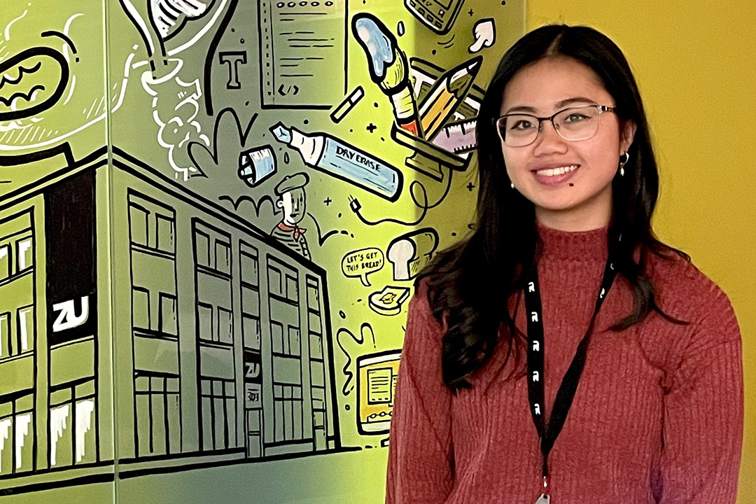 CSPIP Student Chi Vu stands in front of a colourful wall at her employer, zu.